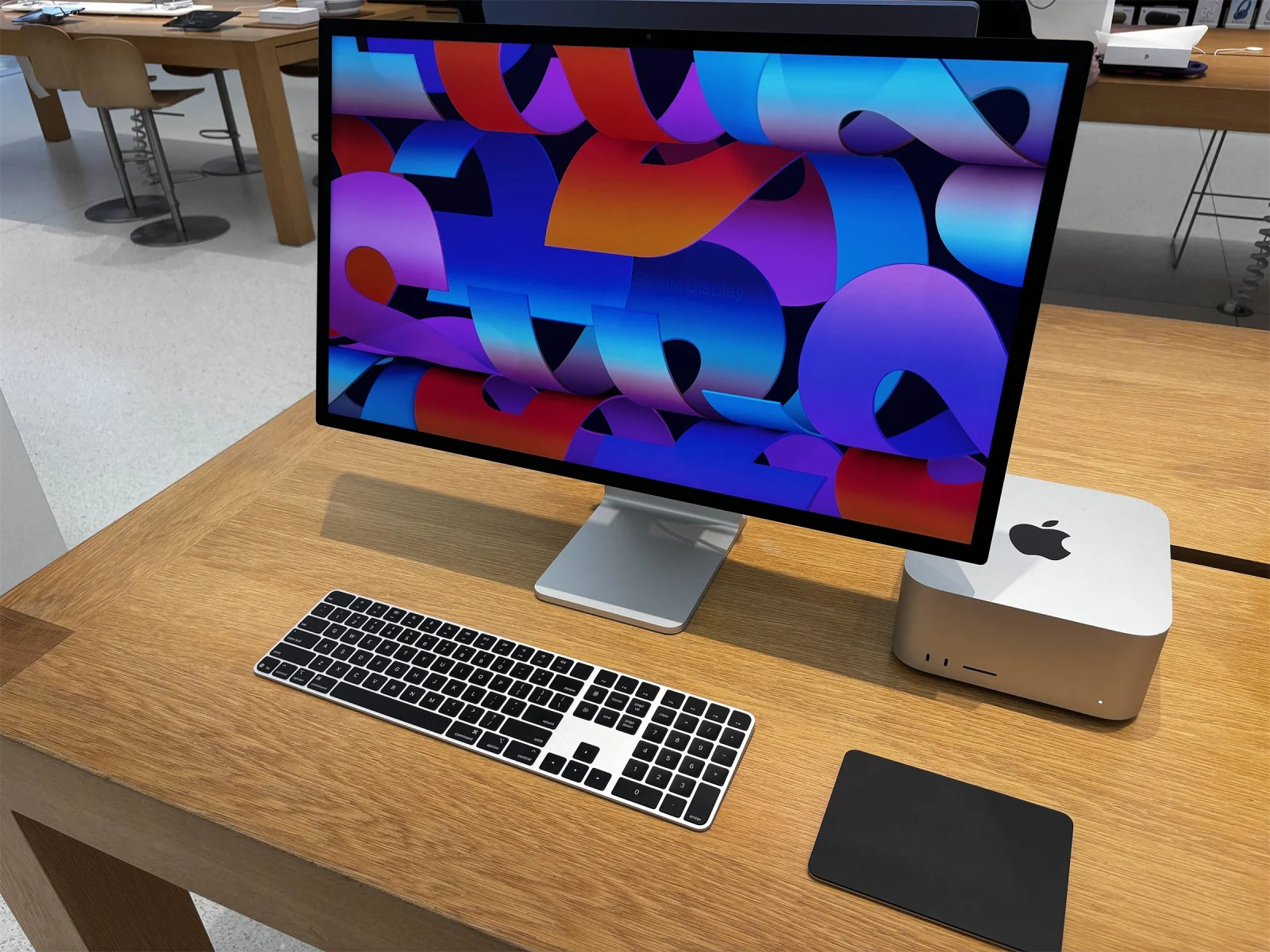 Mac Studio, écran Studio Display, clavier et trackpad noirs posés sur une table en bois