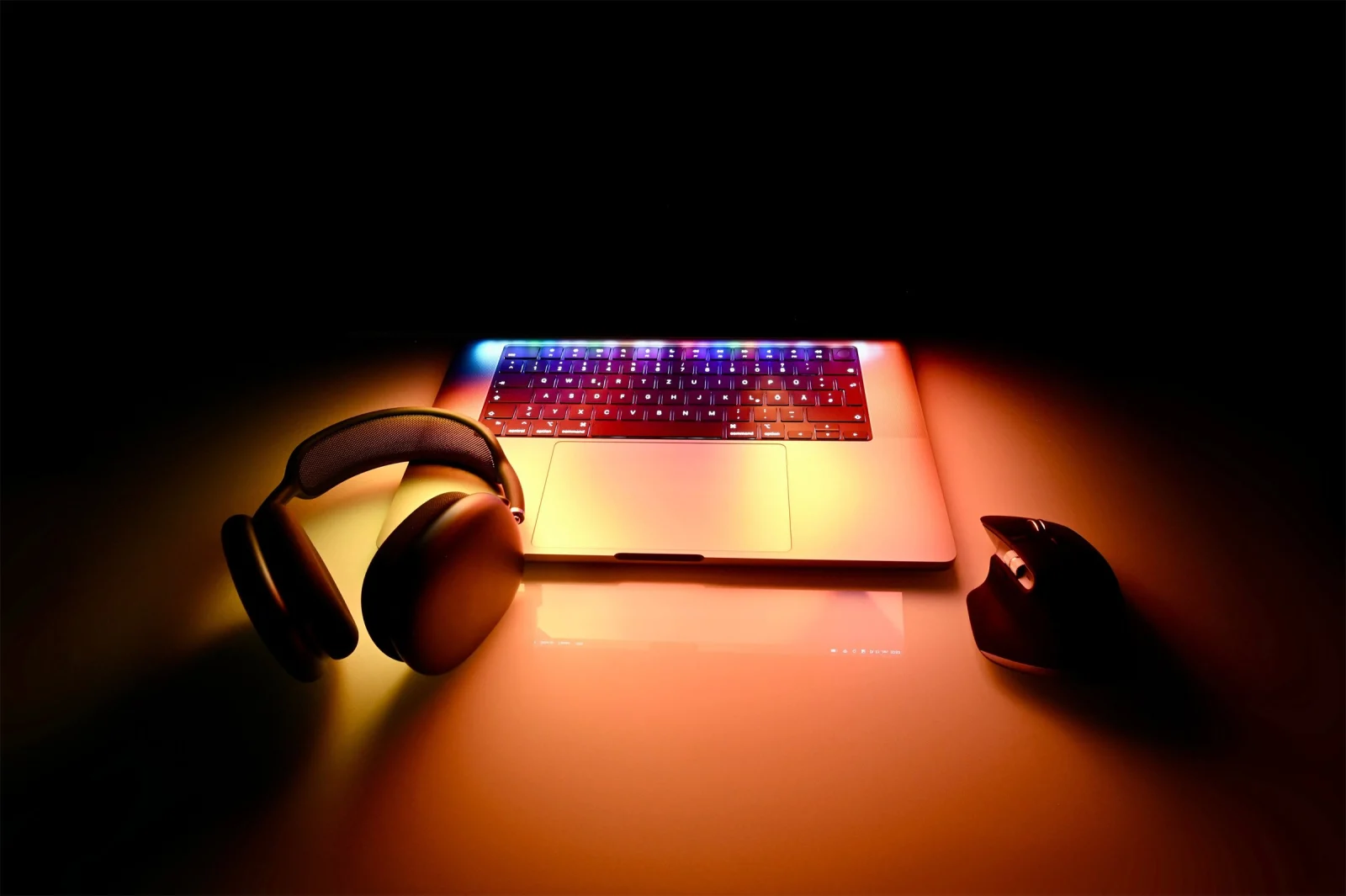 MacBook Pro 16 pouces au clavier rétroéclairé dans la pénombre, entre un casque audio et une souris