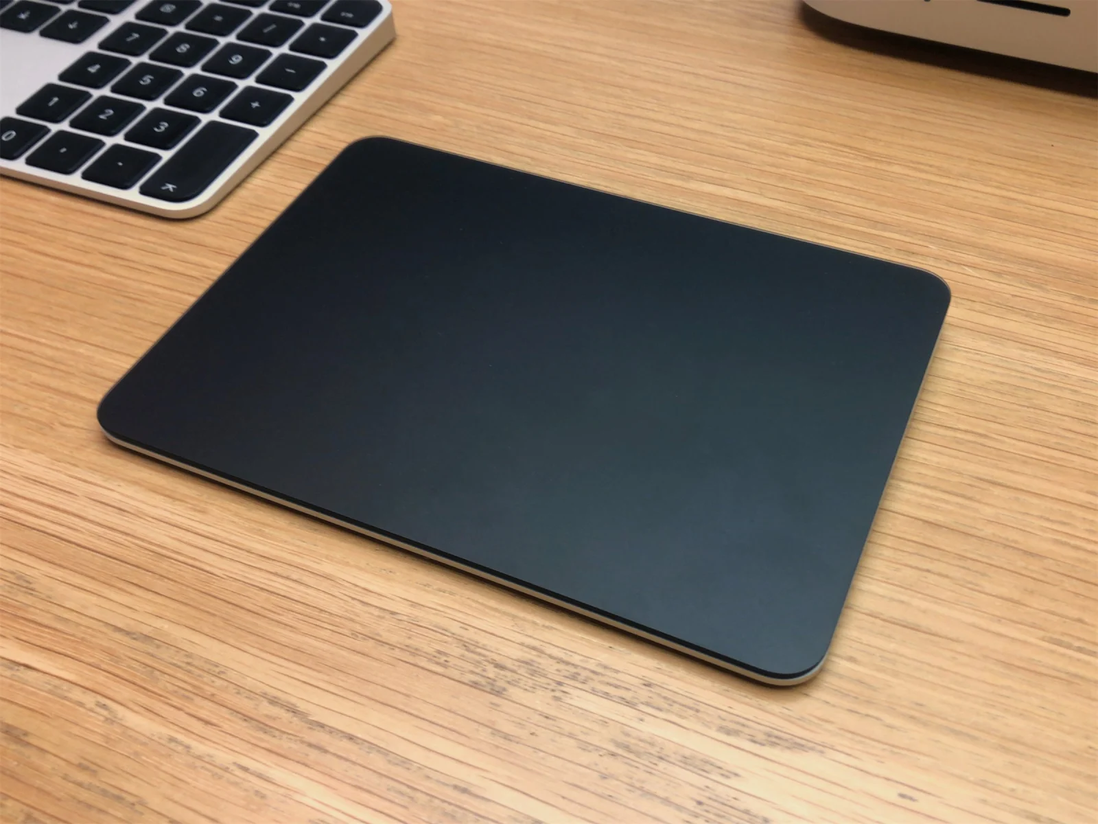 Magic Trackpad noir posé sur un bureau en bois, à côté d'un clavier Apple