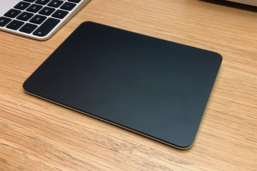 Magic Trackpad noir posé sur un bureau en bois, à côté d'un clavier Apple